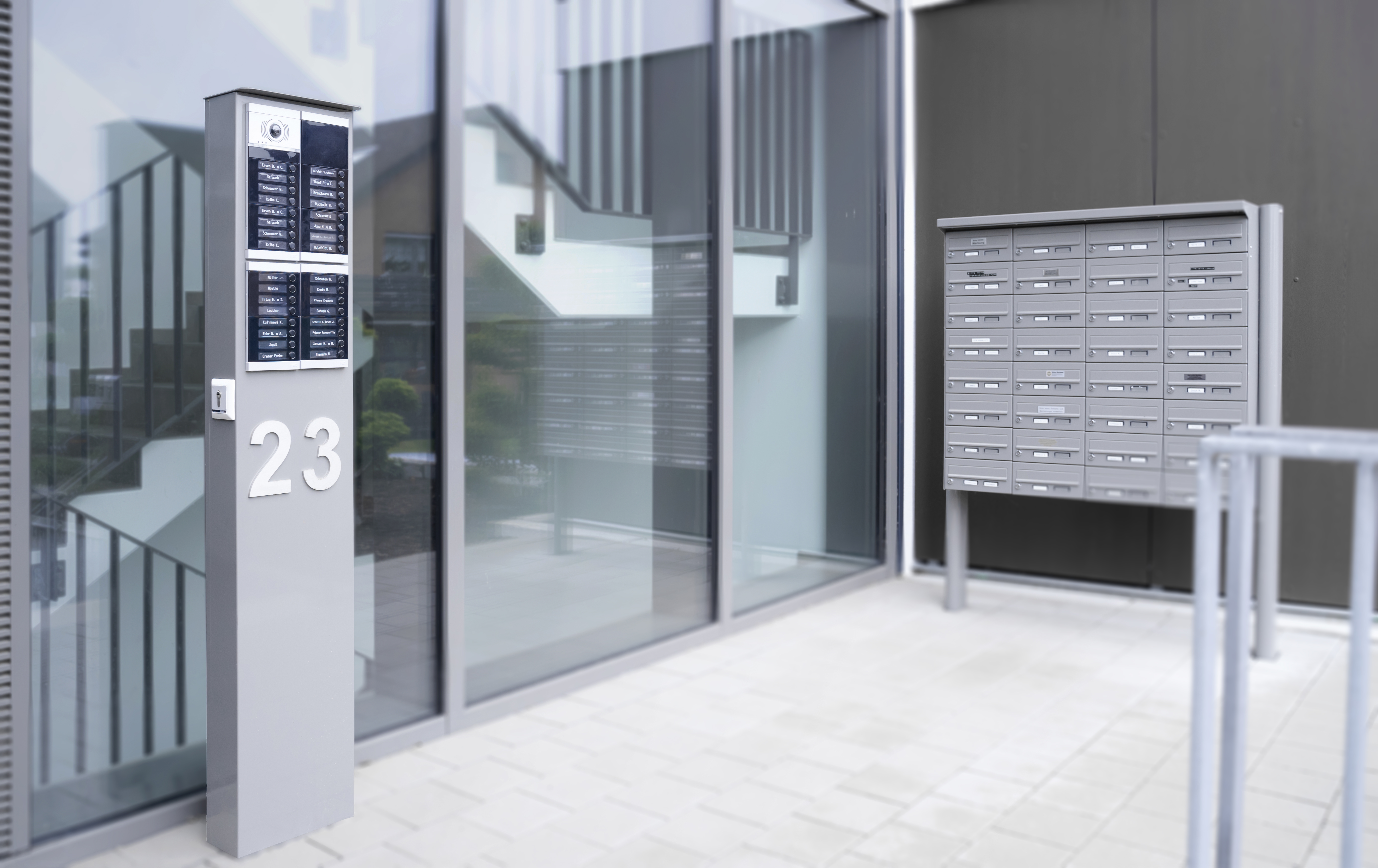 ALPHA-Türstation in Mehrfamilienvariante, eingebaut in eine STele vor einem Hauseingang; daneben steht eine Briefkastenanlage mit vielen Briefkästen