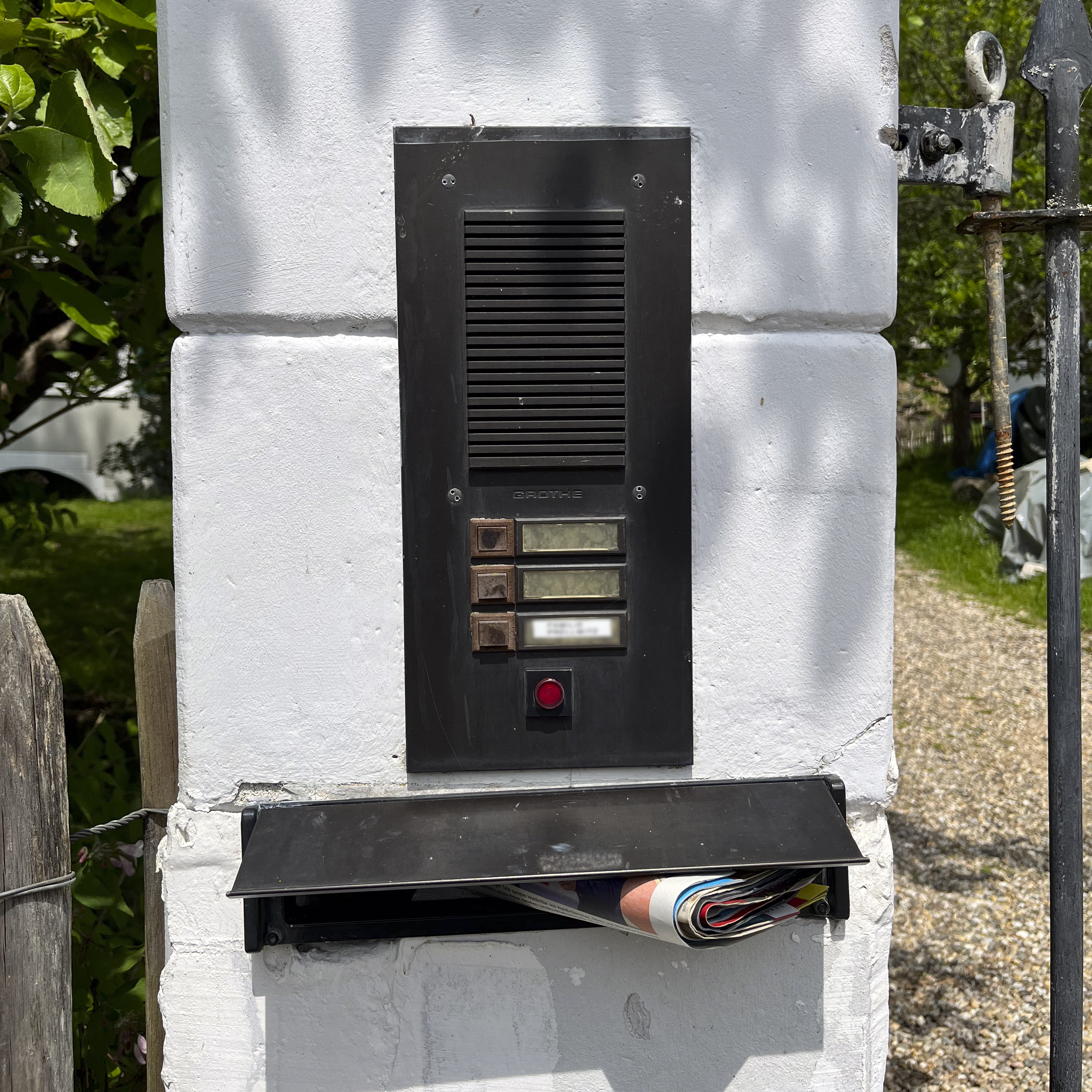 Veraltete Türstation, eingebaut in eine gemauerte Säule vor einem Vorgarten, in einem Rahmen und über einem Briefkastenschlitz