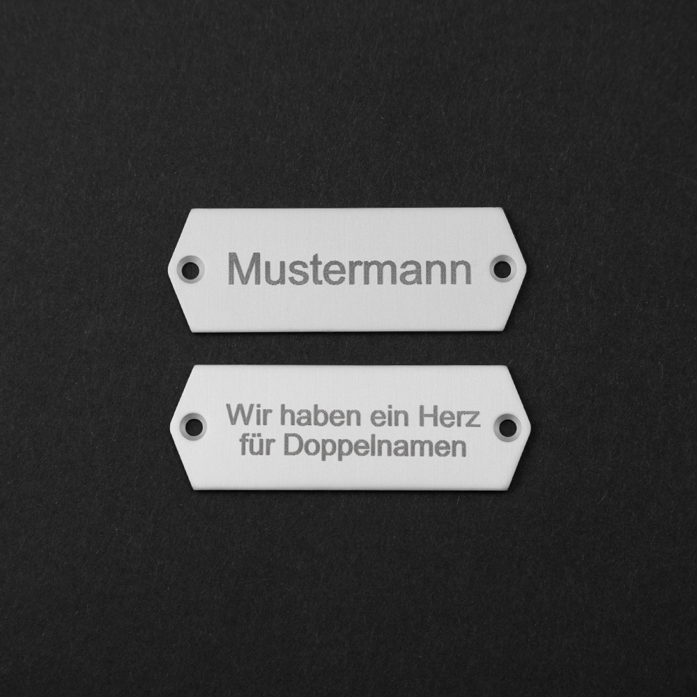 Zwei Edelstahl-Gravierschilder untereinander; auf dem oberen steht "Mustermann", auf dem unteren steht "Wir haben ein Herz für Doppelnamen"