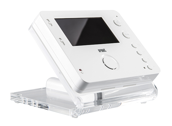 Weißer Videomonitor mit Display, mehreren runden Tasten und runden Lautsprecher, schräg auf transparentem Adapter platziert.