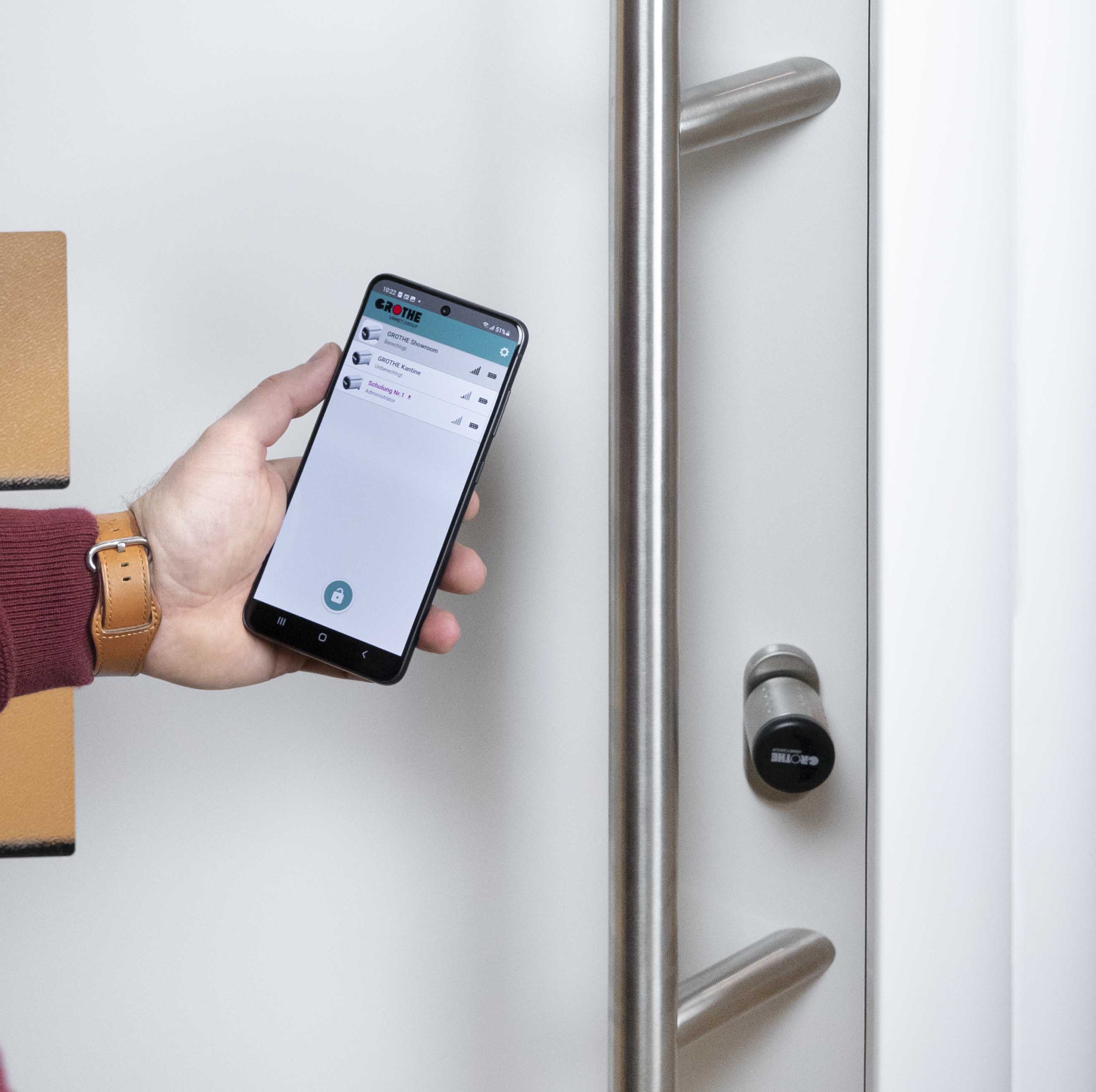 eLock-Schließzylinder eingebaut in eine Tür; davor hält jemand ein Smartphone mit der geöffneten eLock-App