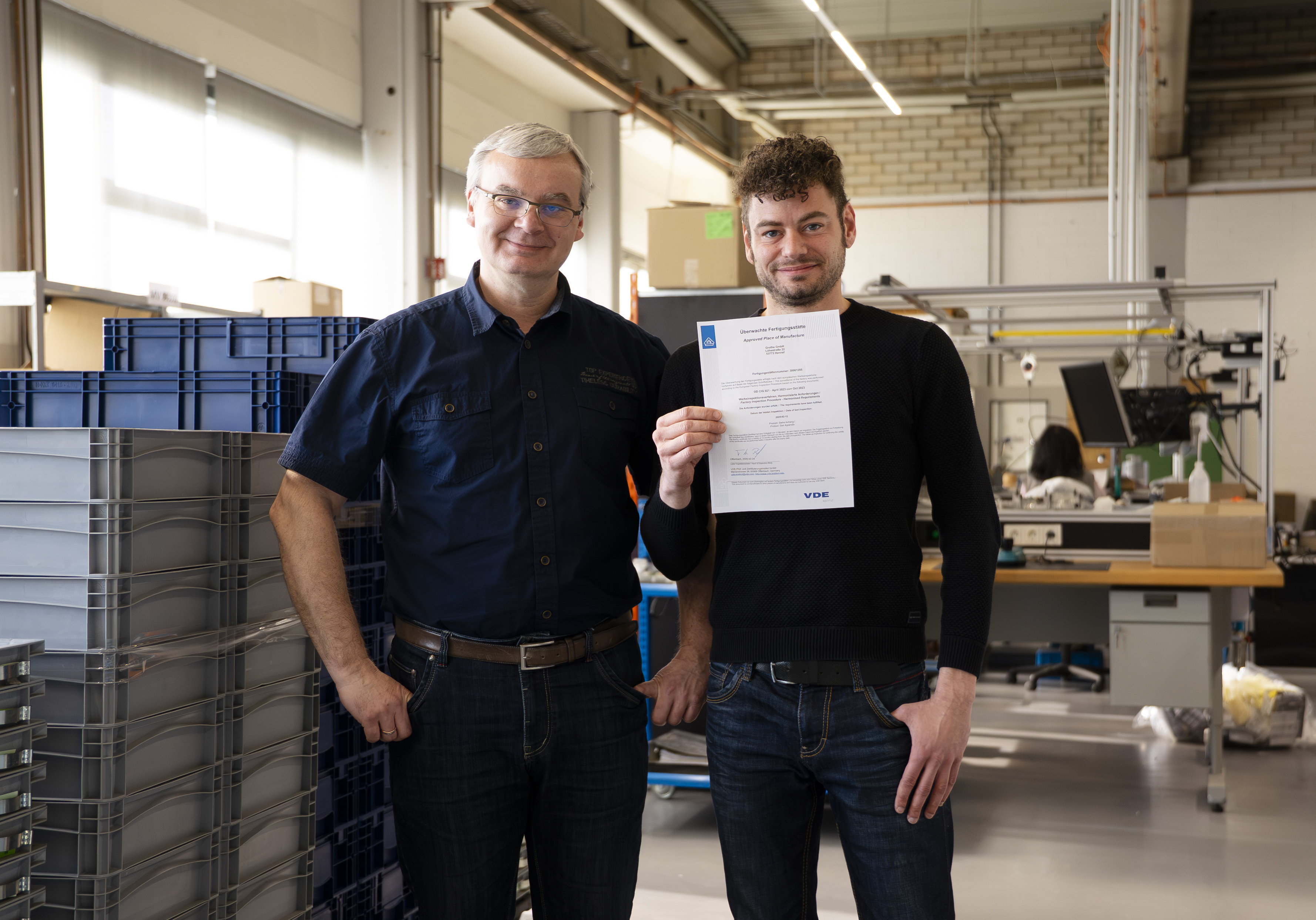 Zwei Grothe-Mitarbeiter blicken freundlich in die Kamera; einer von beiden hält ein Zertifikat in der Hand