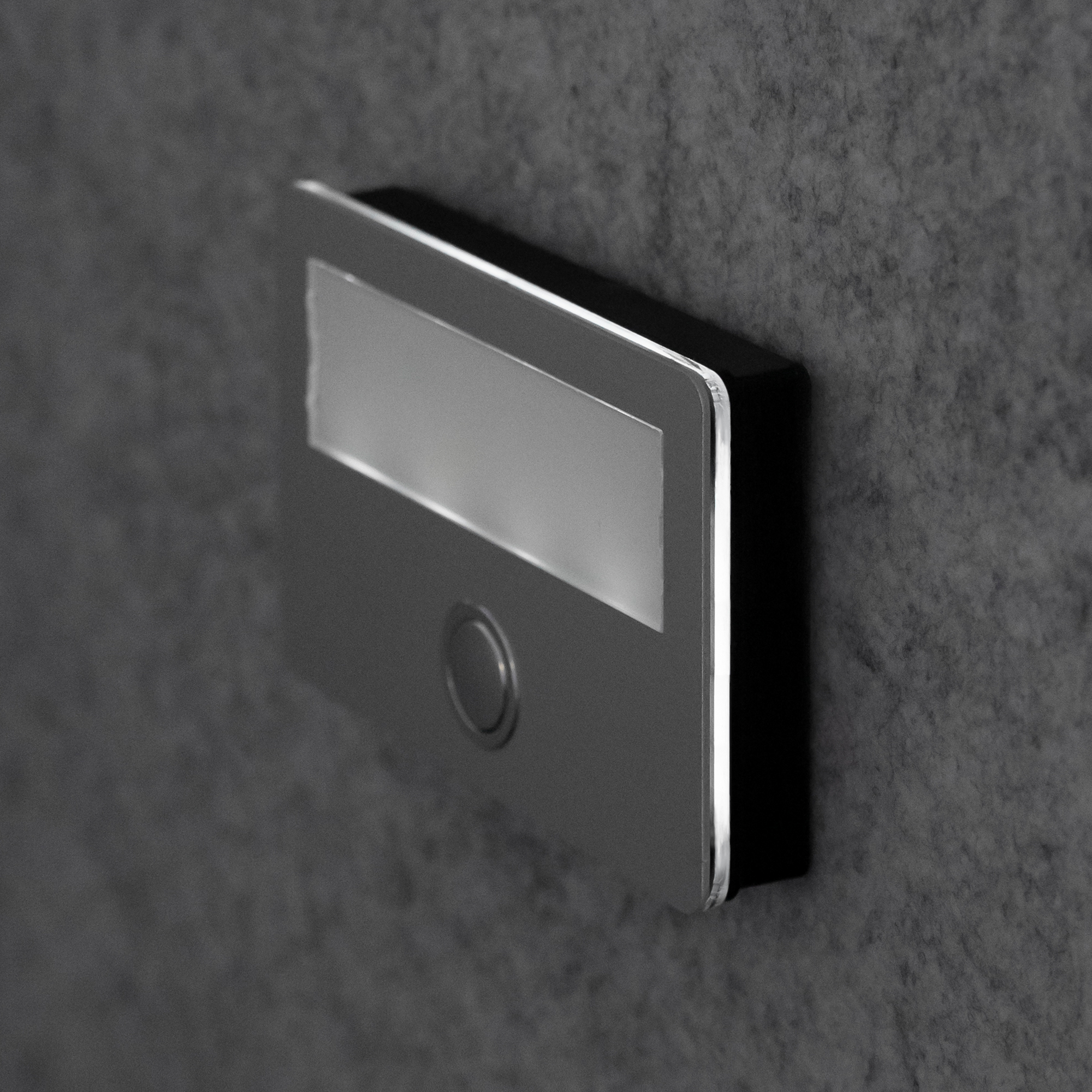 Seitlich beleuchtete Etagenplatte mit rundem Taster und Namensschild, Ansicht von schräg vorne rechts an der Wand.