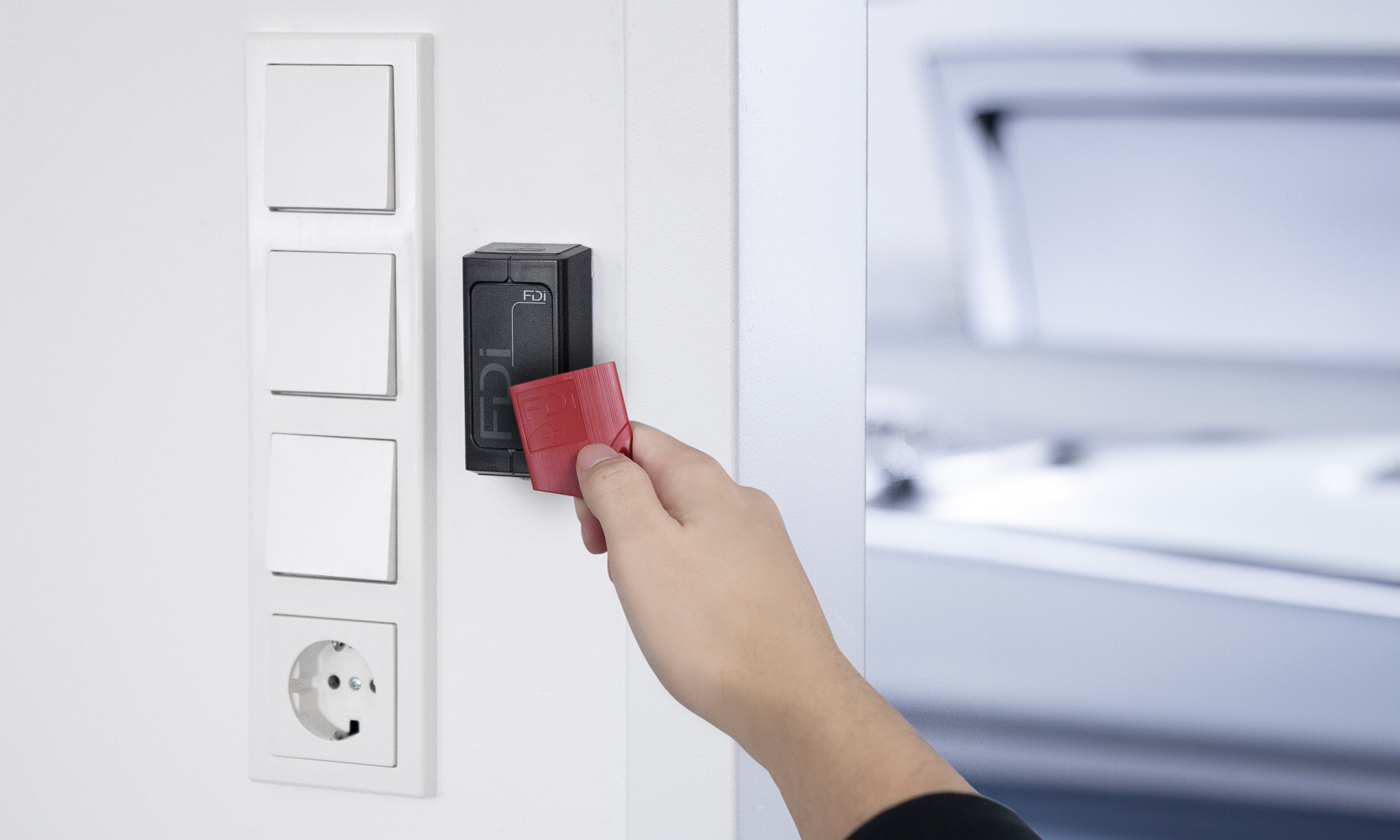 Lesegerät hängt an einer Wand neben einem Schalterprogramm; eine Hand hält einen roten Näherungsschlüssel vor das Lesegerät