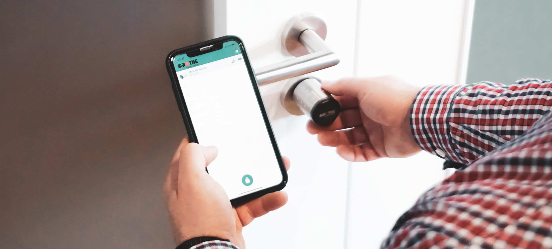 Türschloss mit eingebautem eLock-Schließzylinder und einer Hand, die ein Smartphone mit geöffneter eLock-App davorhält