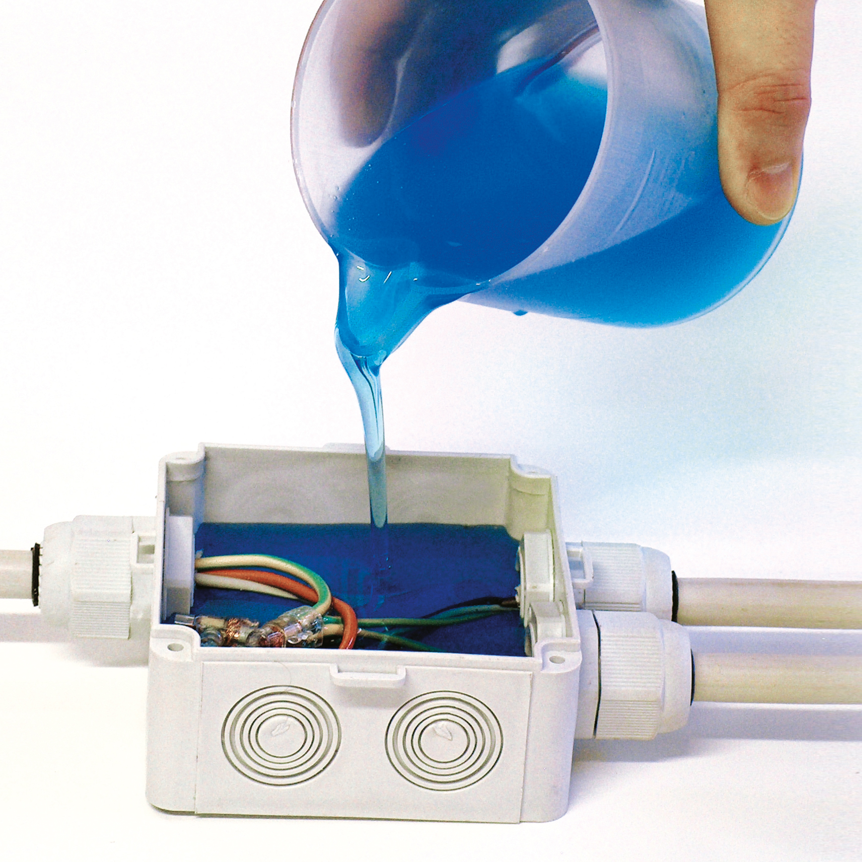 Eine Verteilerdose mit innenliegenden kleineren Kabeln wird mit dem Zweikomponenten-Gel aus dem Becher gefüllt