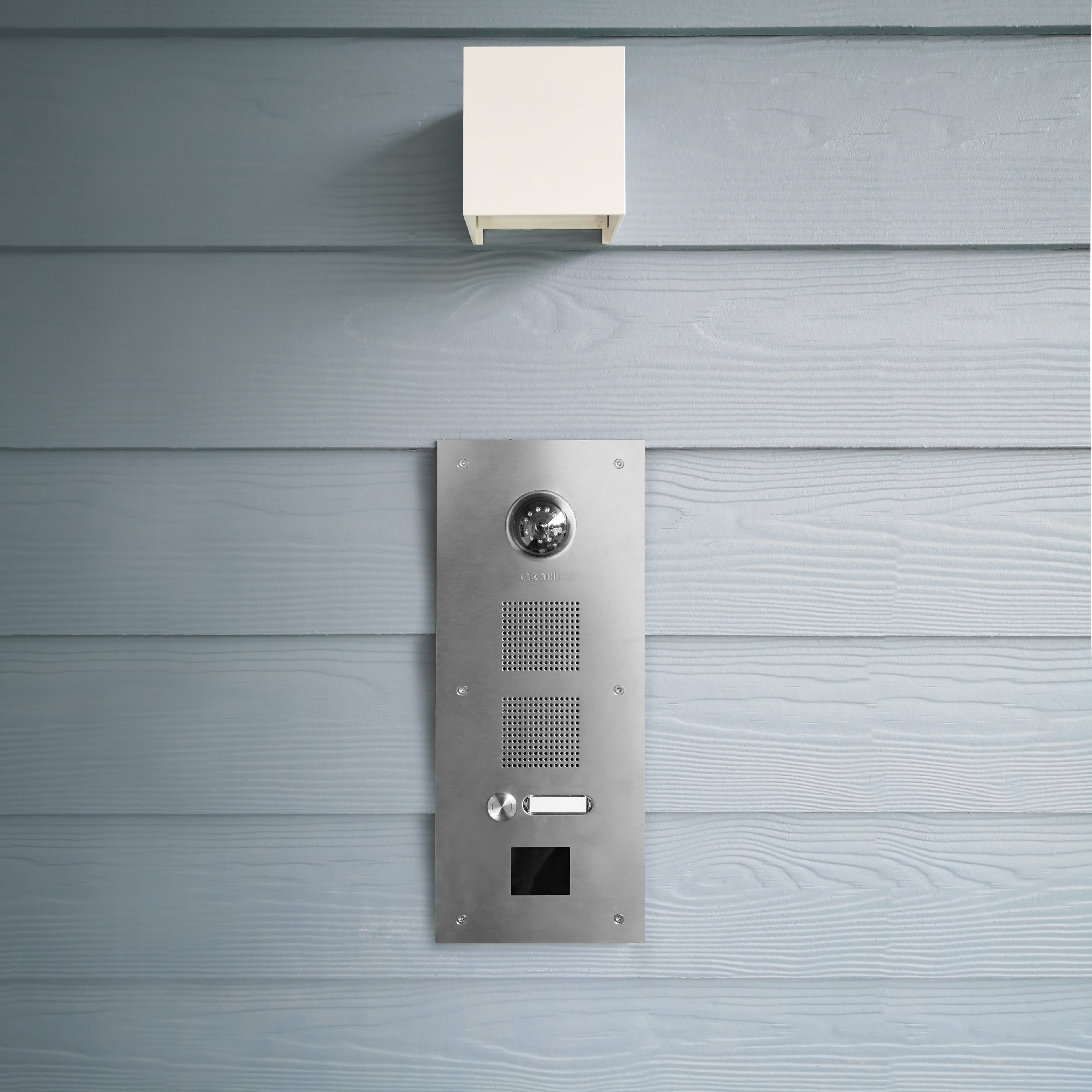 ROBUSTA-Video-Türstation, angebracht an einer Holzfassade; darüber hängt eine Leuchte