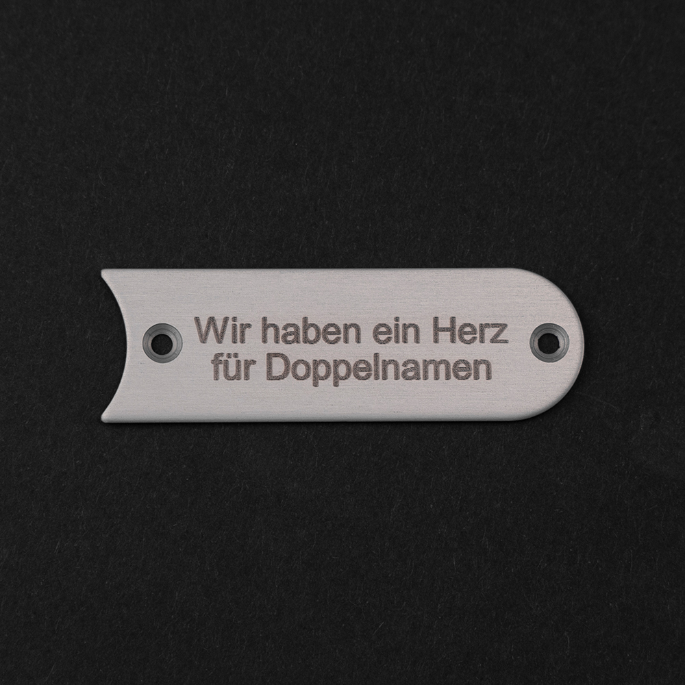 Edelstahl-Gravierschild seitlich liegend; darauf steht "Wir haben ein Herz für Doppelnamen"