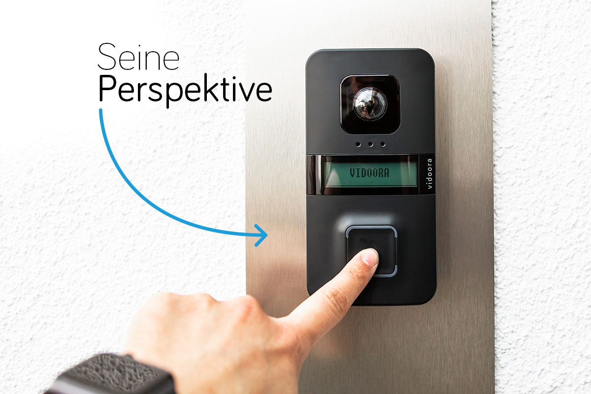 vidoora hängt an einer Fassade; ein Finger drückt auf den Taster, an einem Pfeil steht "Seine Perspektive"
